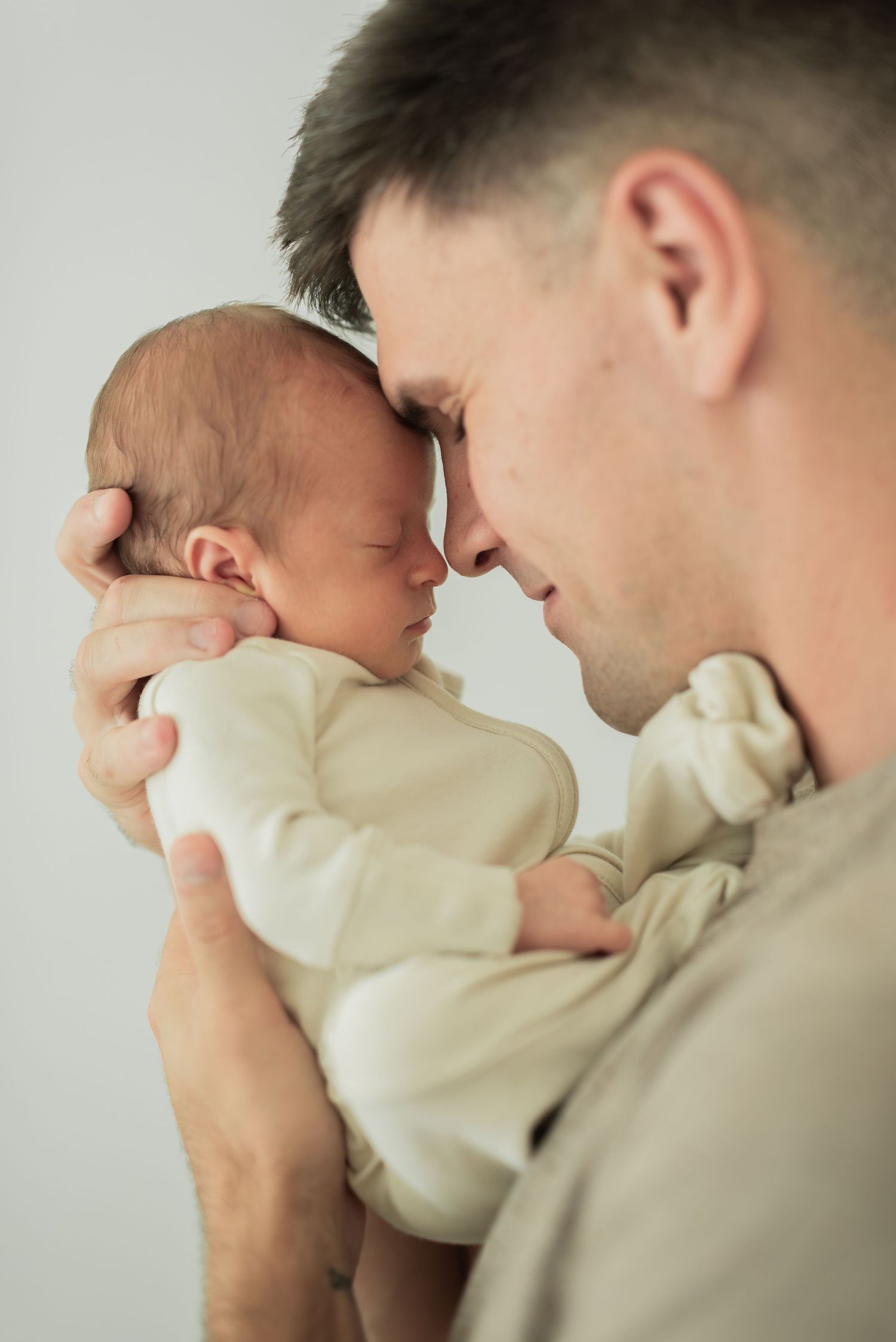 army dad holding baby son up to his face. nose to nose. scrunched up, eyes closed. at home newborn session
