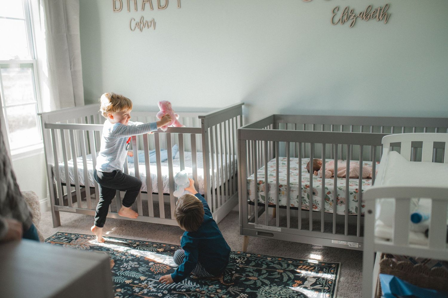 twin boys playing in nursery on crib, with teddy bears, newborn twins