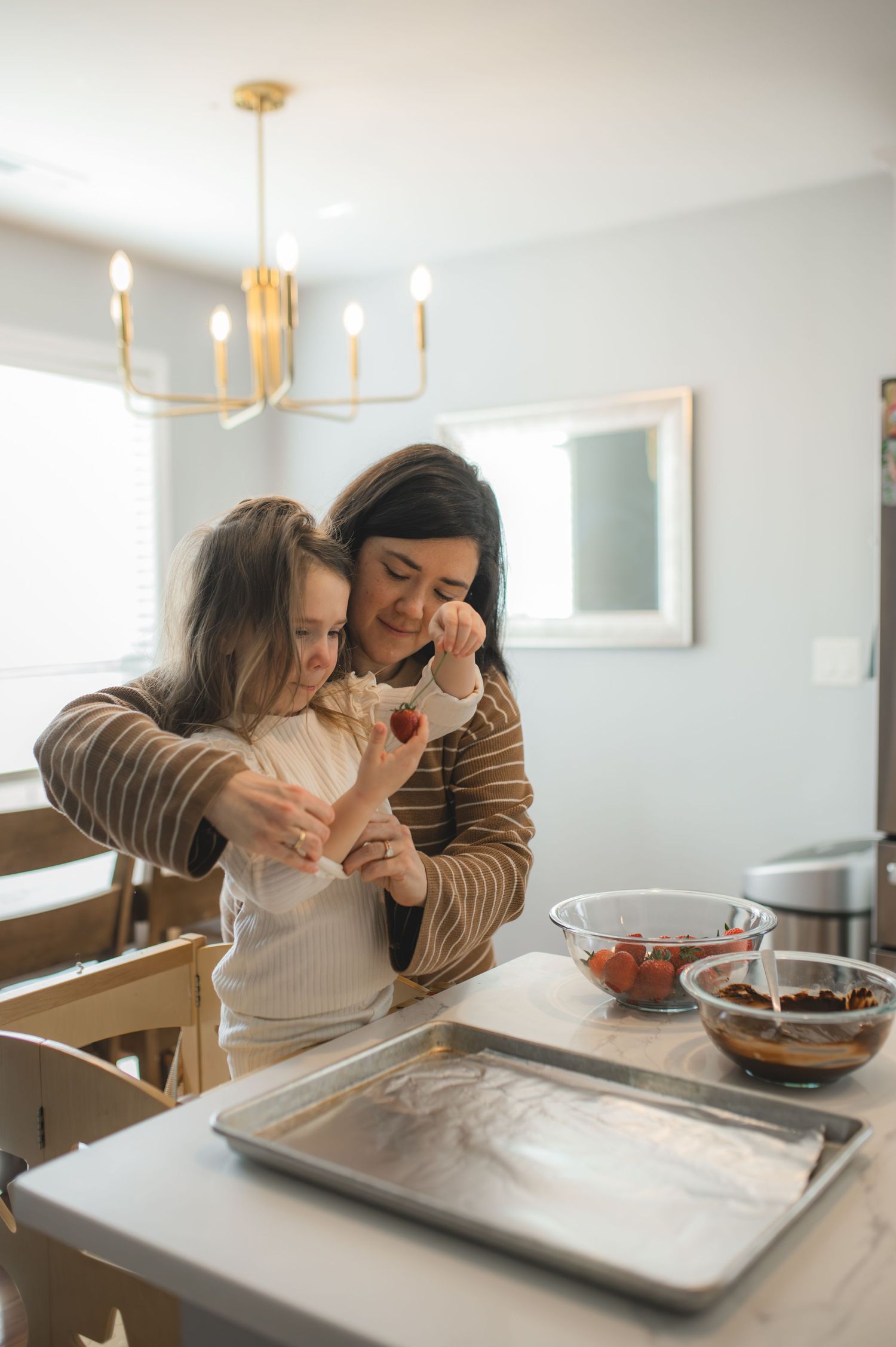 mom and daughter rolling up sleeves to dip strawberries into chocolate in kitchen, greenville, nc