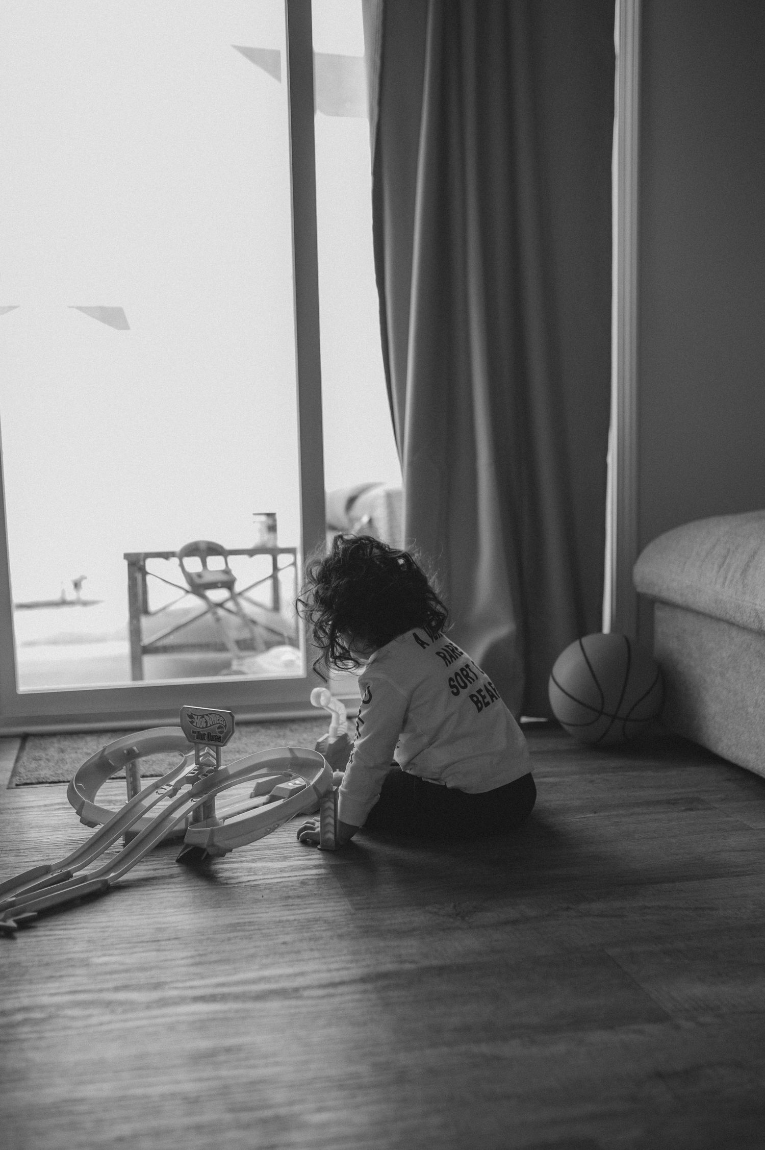child playing with hot wheels car race track on floor in front of glass door window