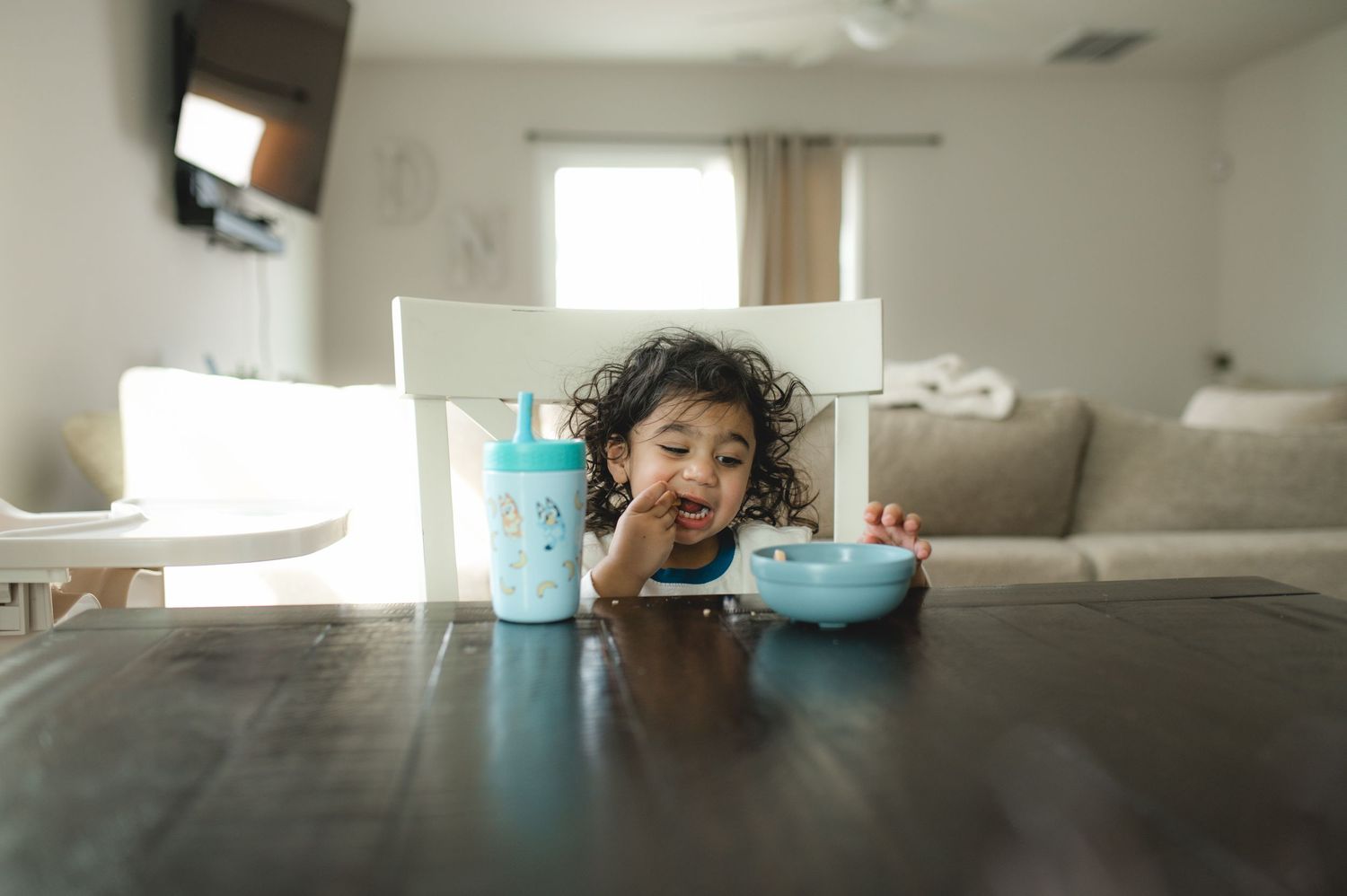 child eating a snack at table with blue bowl and bluey straw cup