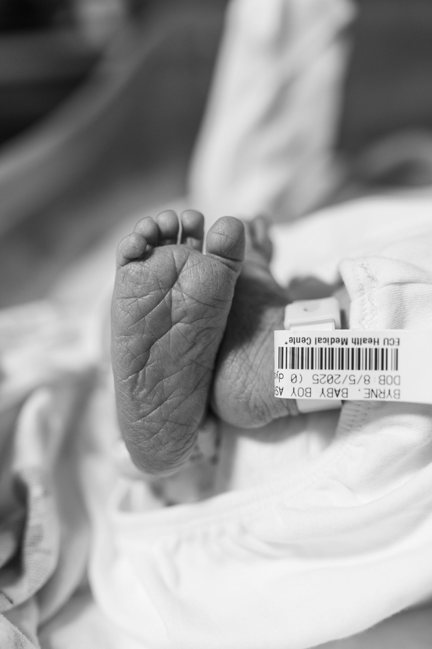 newborn baby after birth in hospital at ECU Health Medical Center in Greenville, NC birth photographer. wrinkly feet. black and white photo.