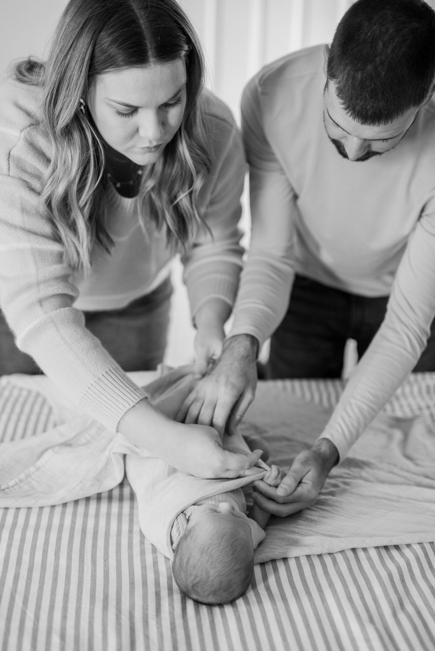 mom and dad swaddling newborn baby on bed at home during documentary style session