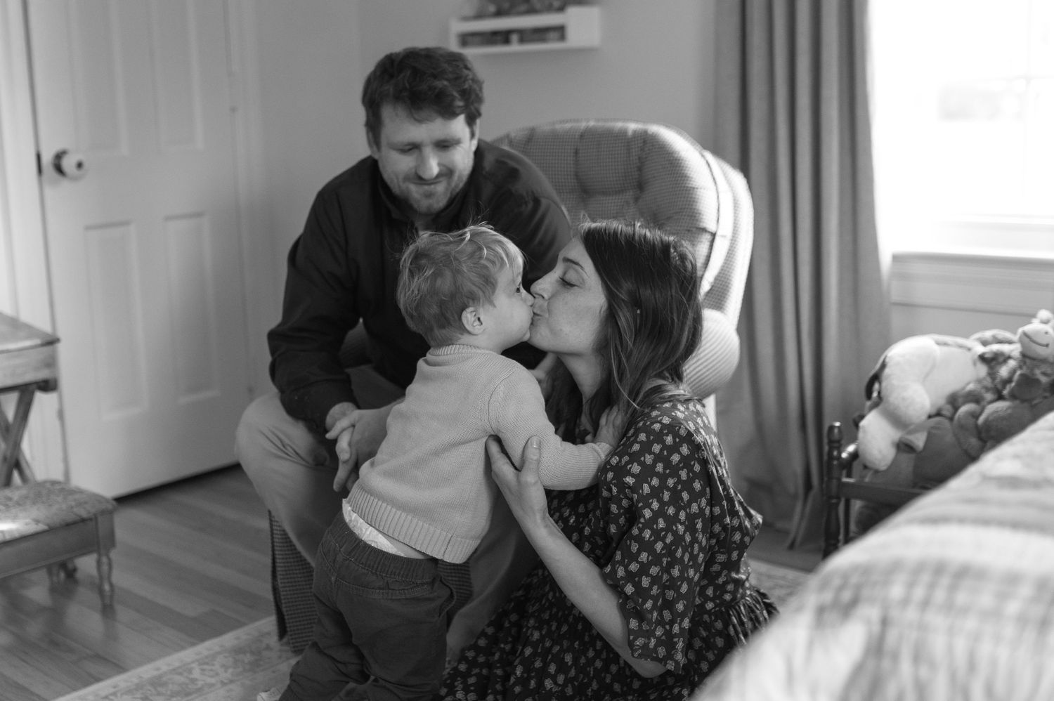 mom dad and toddler sitting on floor playing with toys. at home documentary family maternity session. kissing smiling hugging
