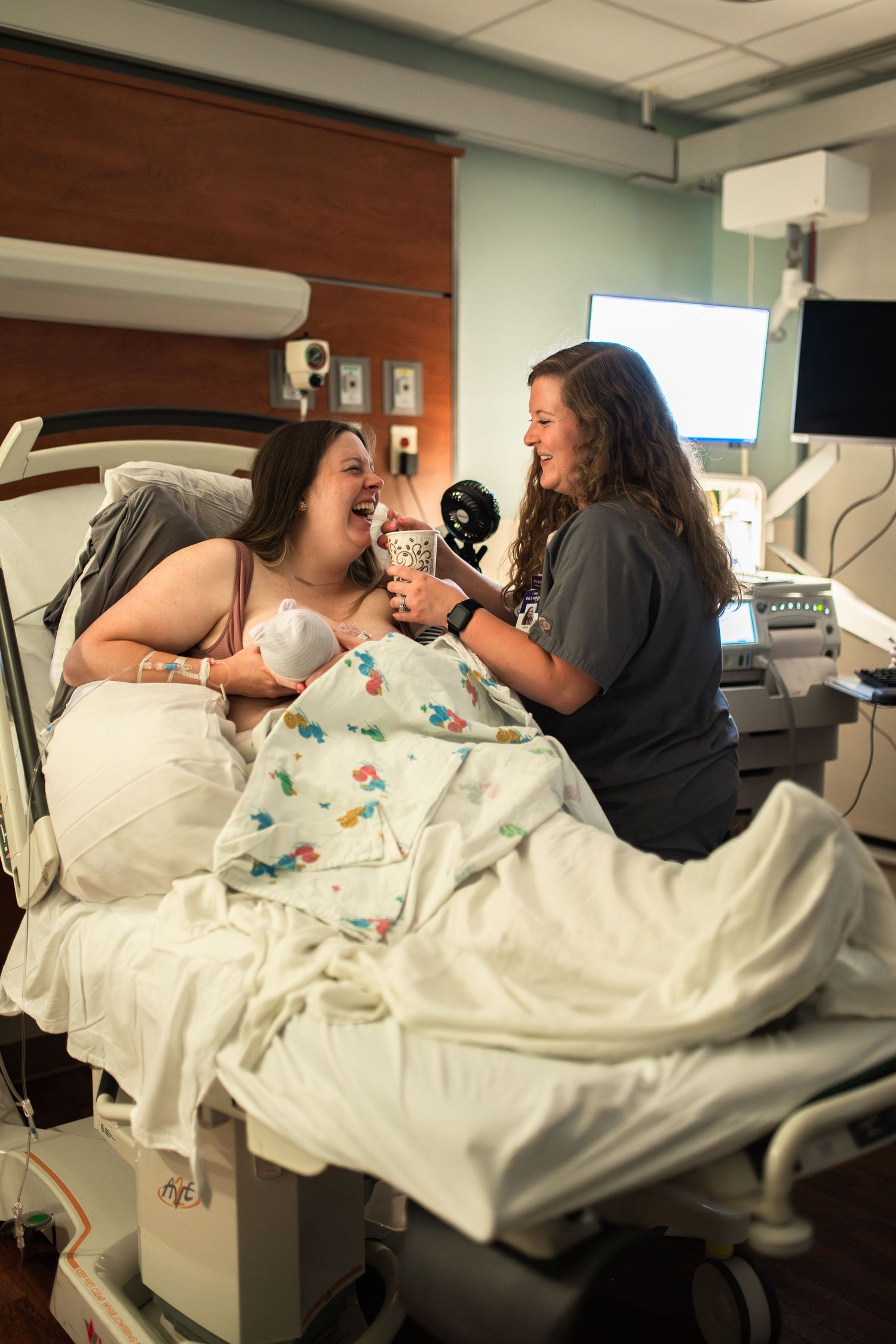 mom breastfeeding baby after birth in hospital at ECU Health Medical Center for the first time with nurse giving mother a drink laughing