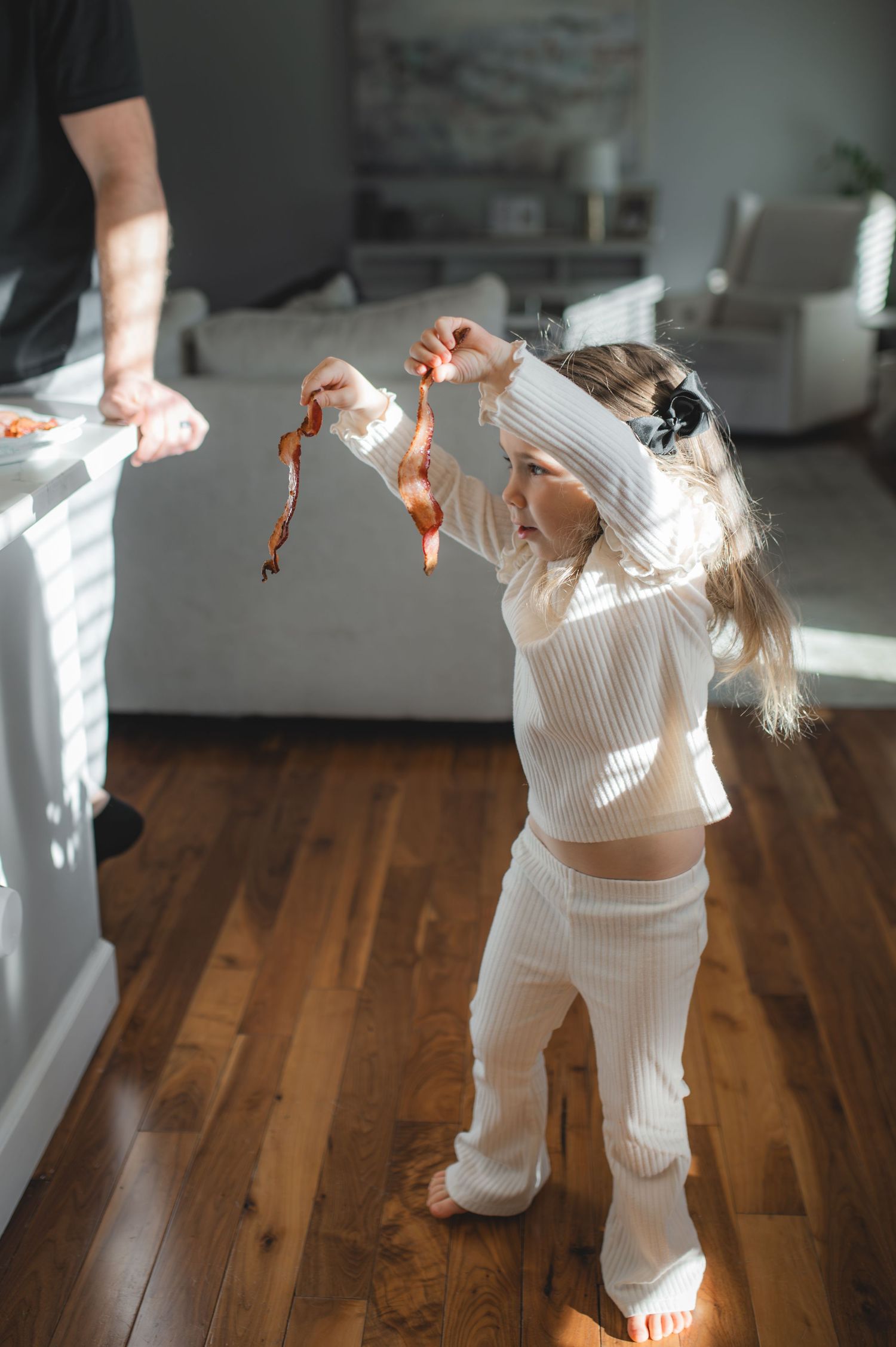 little girl holding slices of bacon dancing in kitchen, greenville, nc
