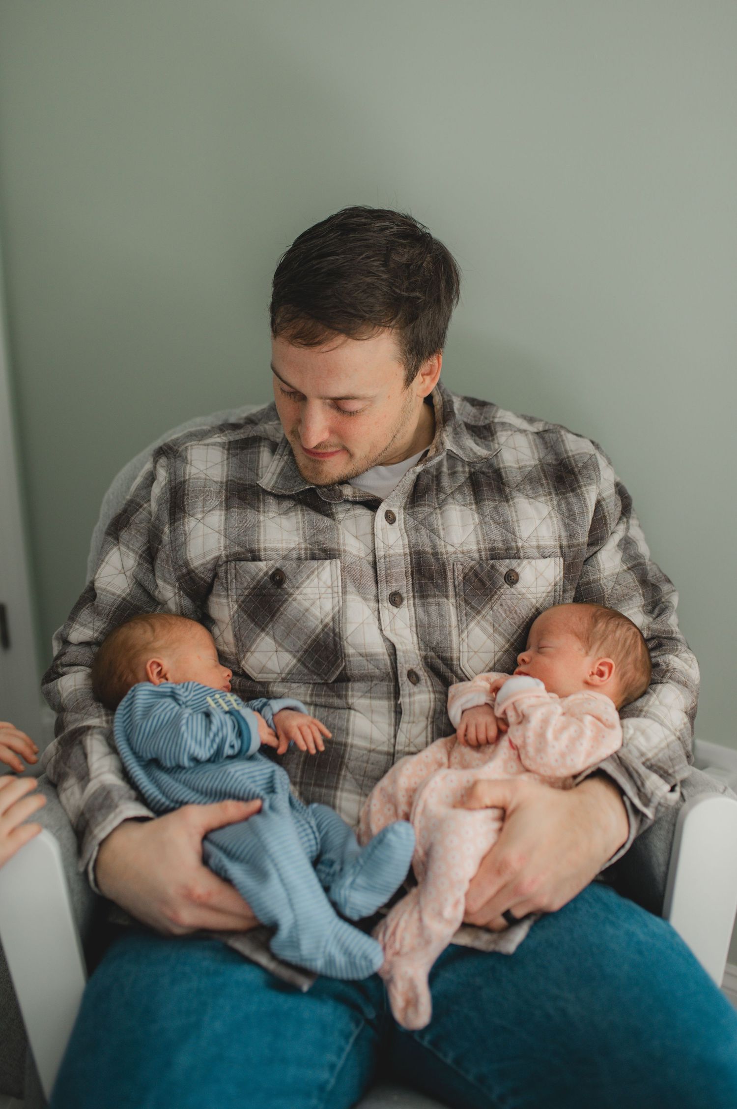dad holding newborn twin boy and girl in rocking chair in nursery