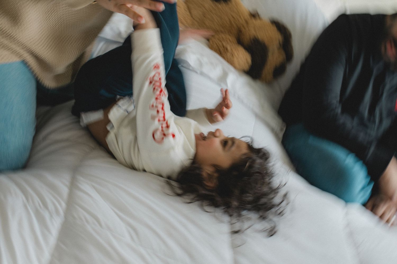 mom dad and son jumping on bed, holding hands, playing, laughing, smiling