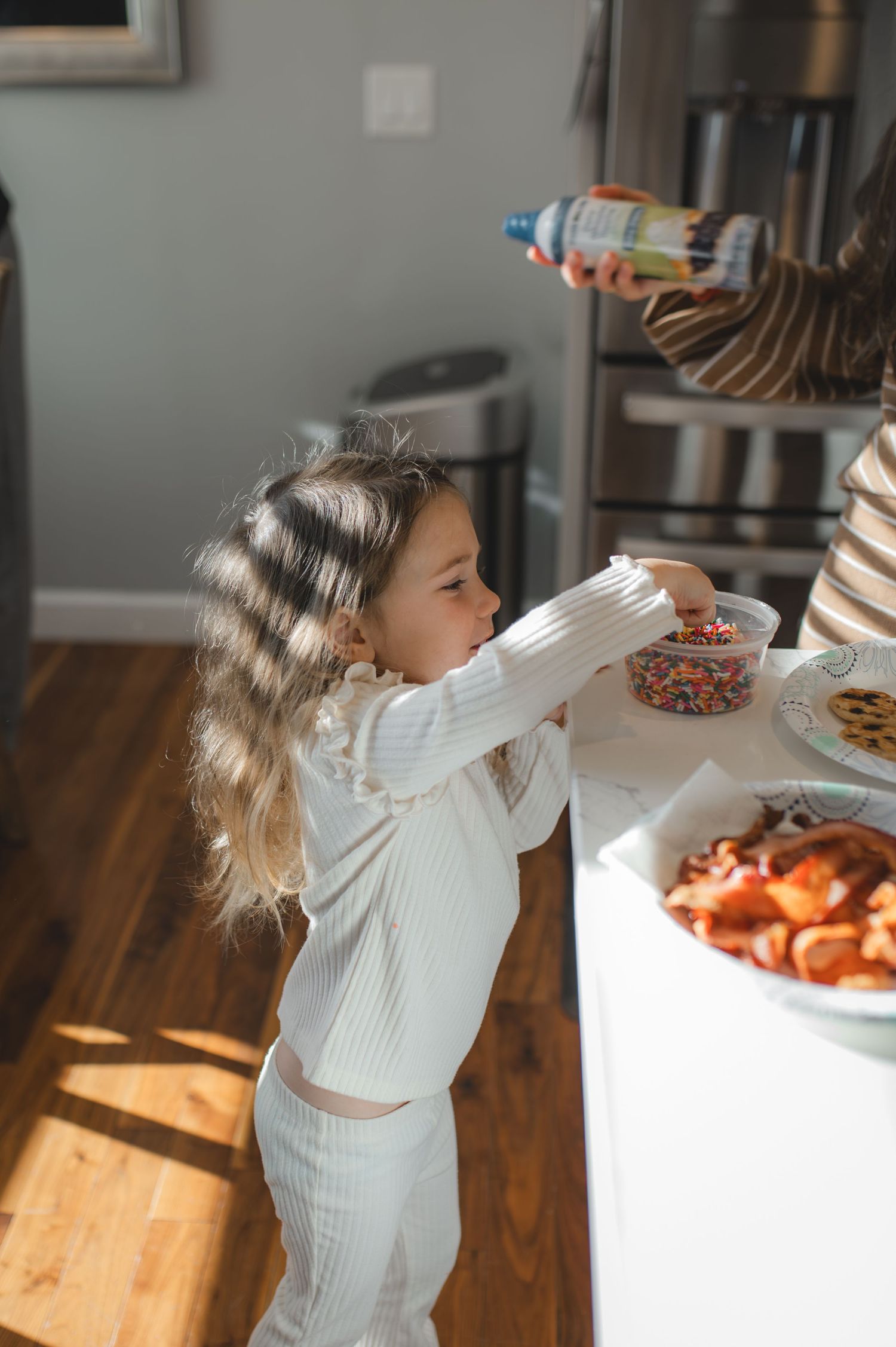 little girl reaching into sprinkles container on counter in kitchen, greenville, nc