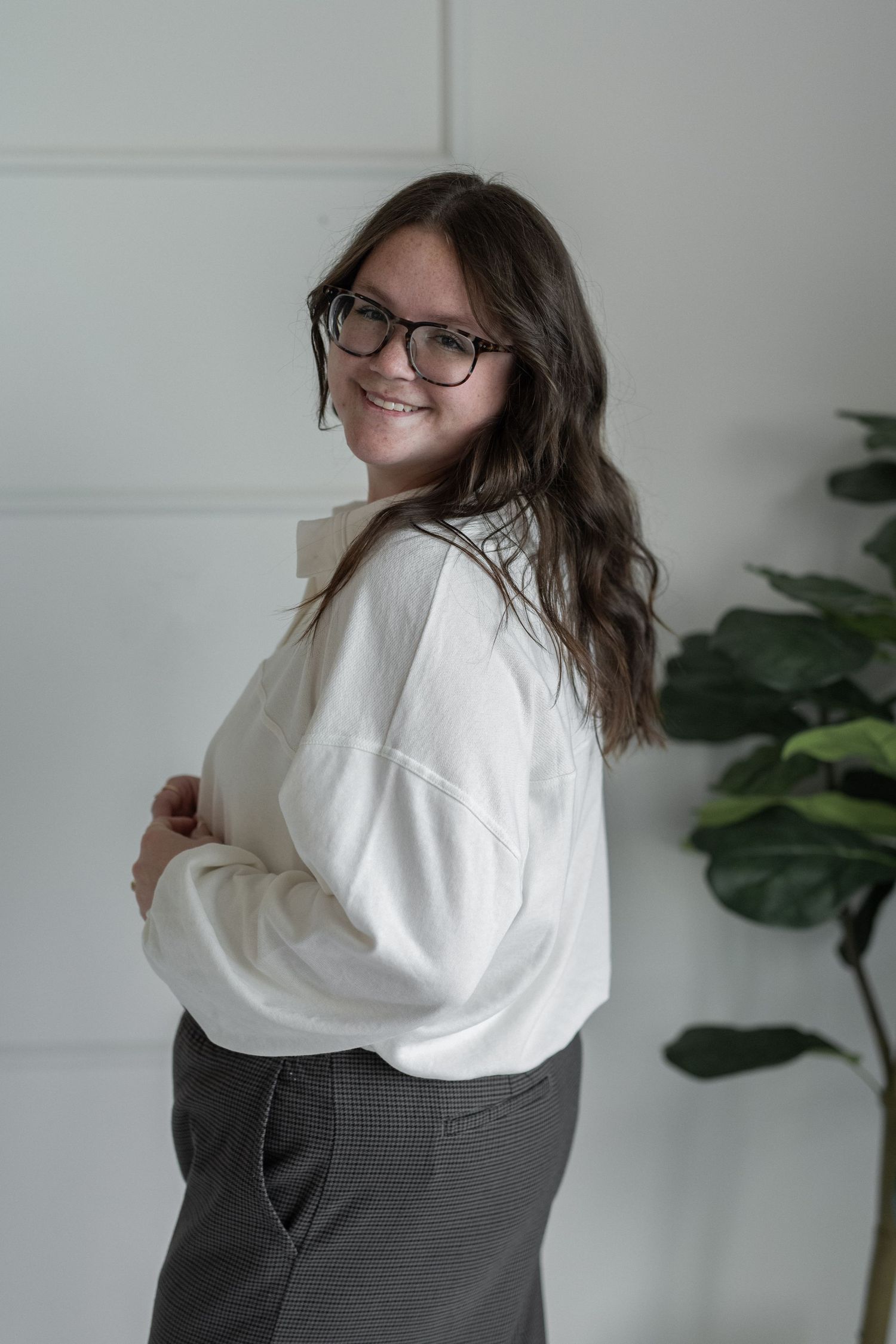woman smiling at the camera. business casual outfit. long brown hair. fiddle-leaf fig tree in the background.