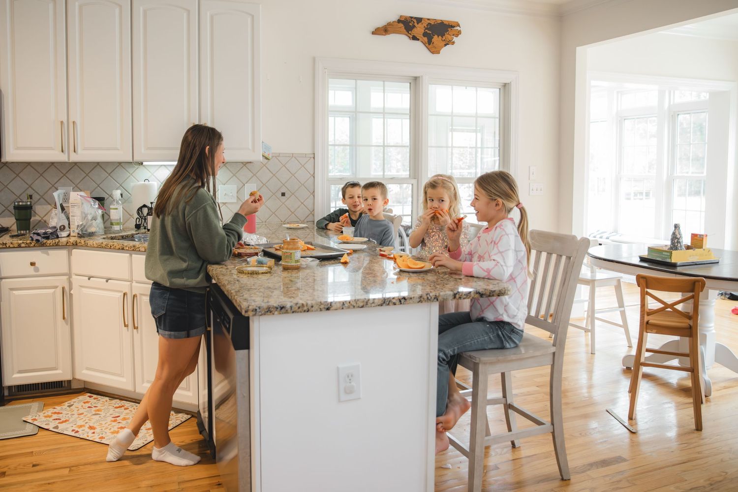 mom and four children sitting at counter eating hummus, carrots, apples, crackers, ranch, cheese