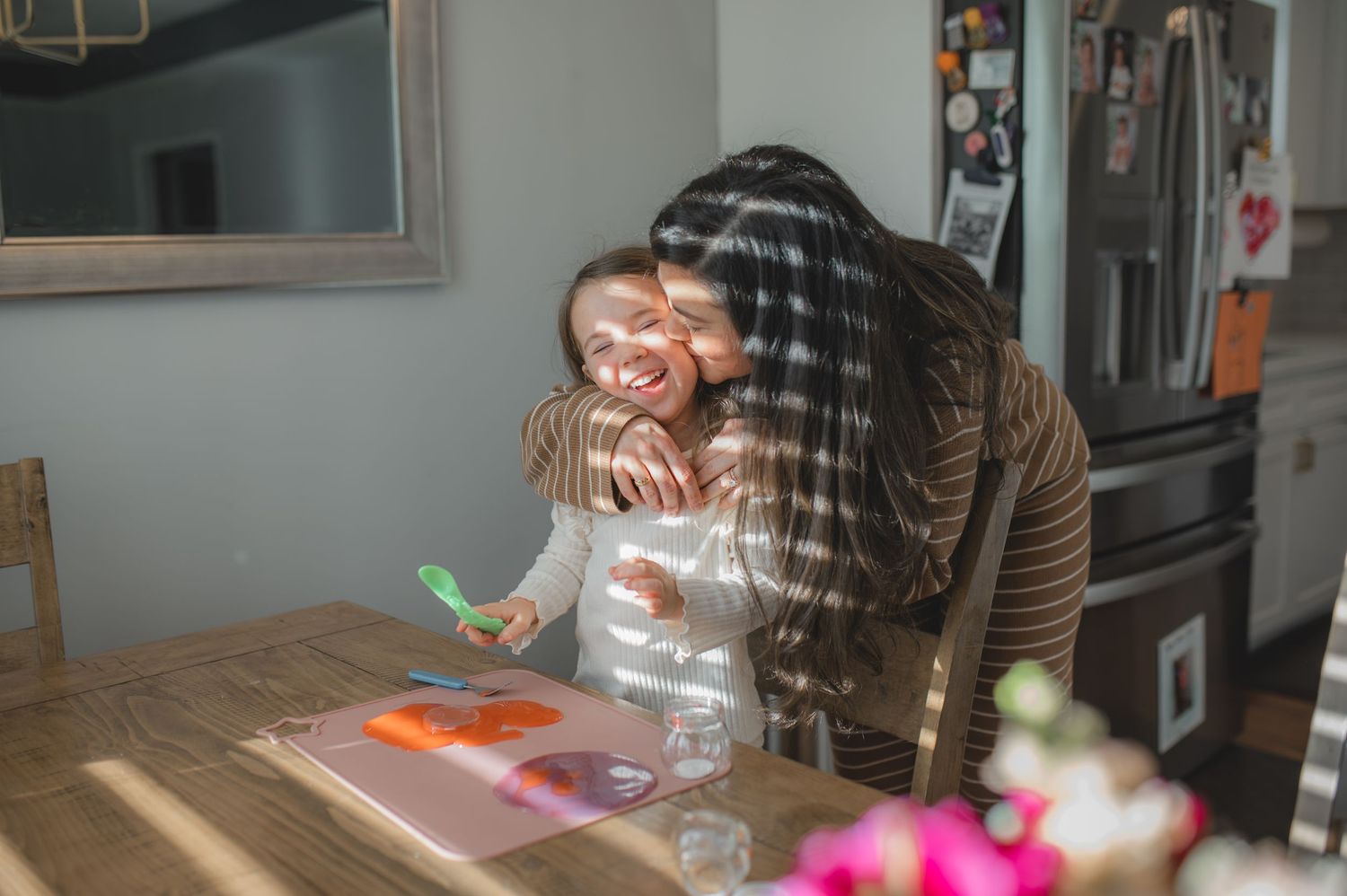 mom and daughter, hugging, playing with slime at kitchen table, sunlight