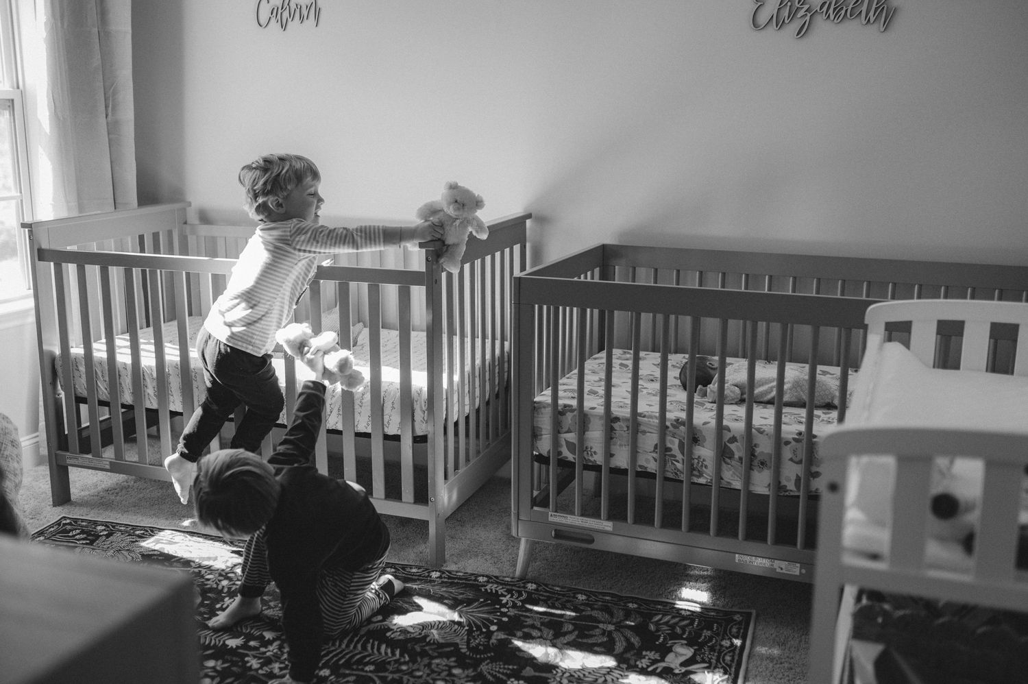 twin boys playing in nursery by crib and newborn twins