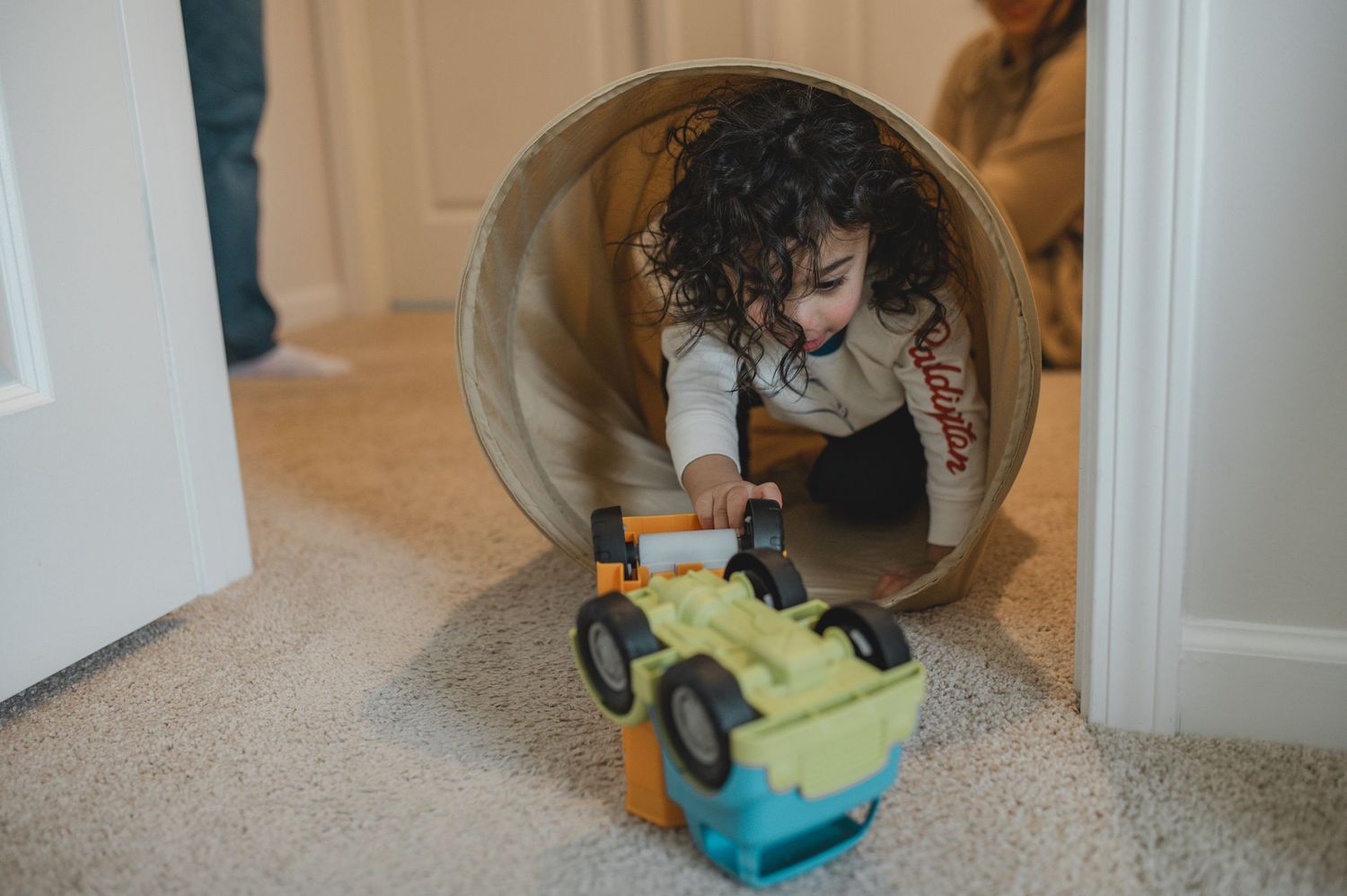 child pushing dump truck toy through play fabric tunnel