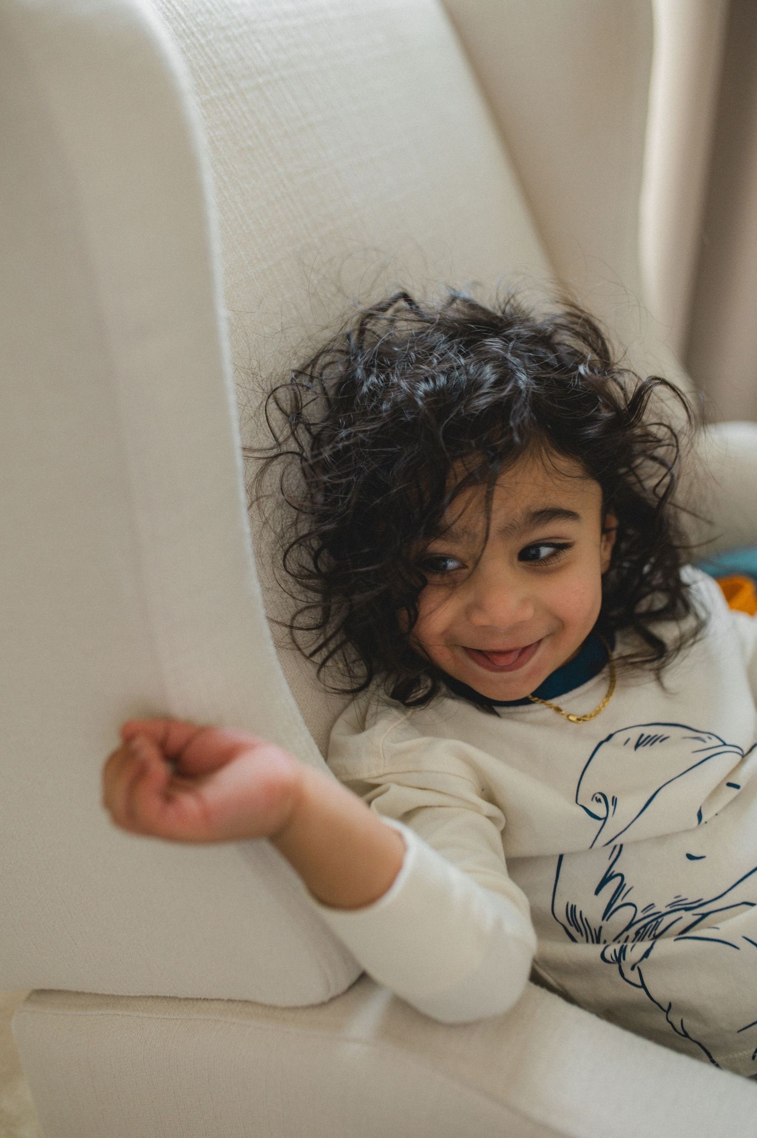 child sitting in rocking chair, laughing, holding hand up, curly hair