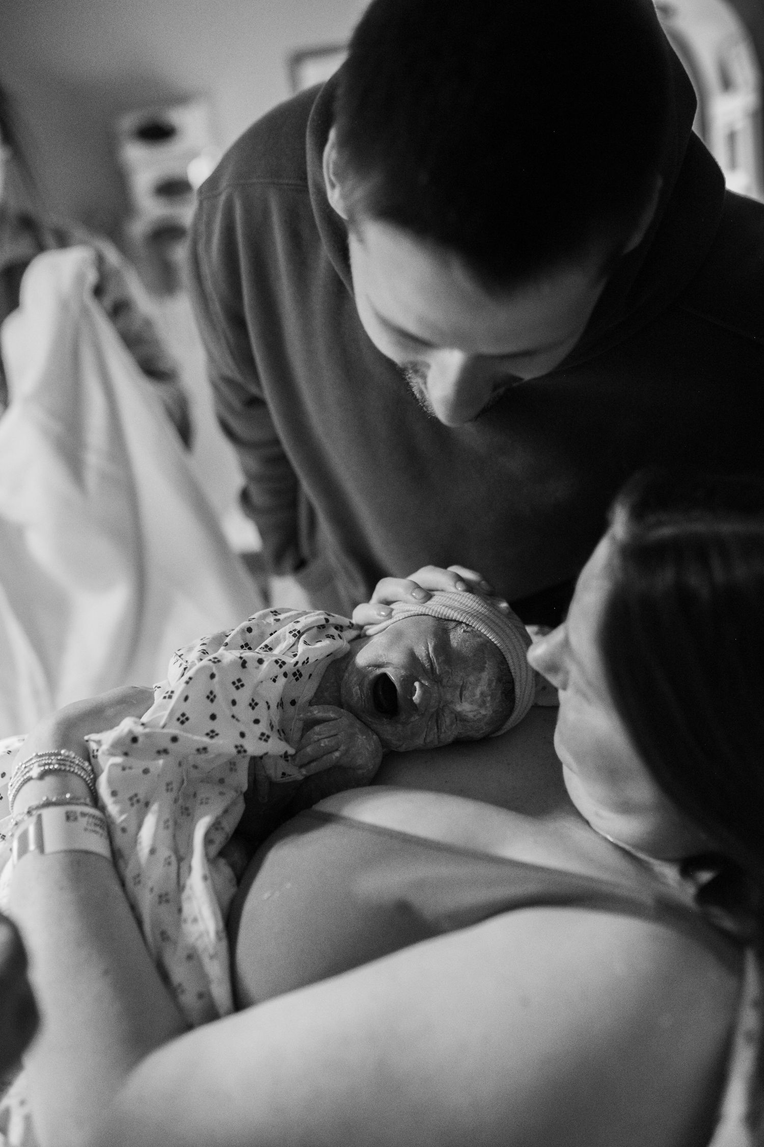mom and dad looking at baby after birth at ECU Health Medical Center in Greenville NC. baby on mothers chest crying laughing smiling hugging