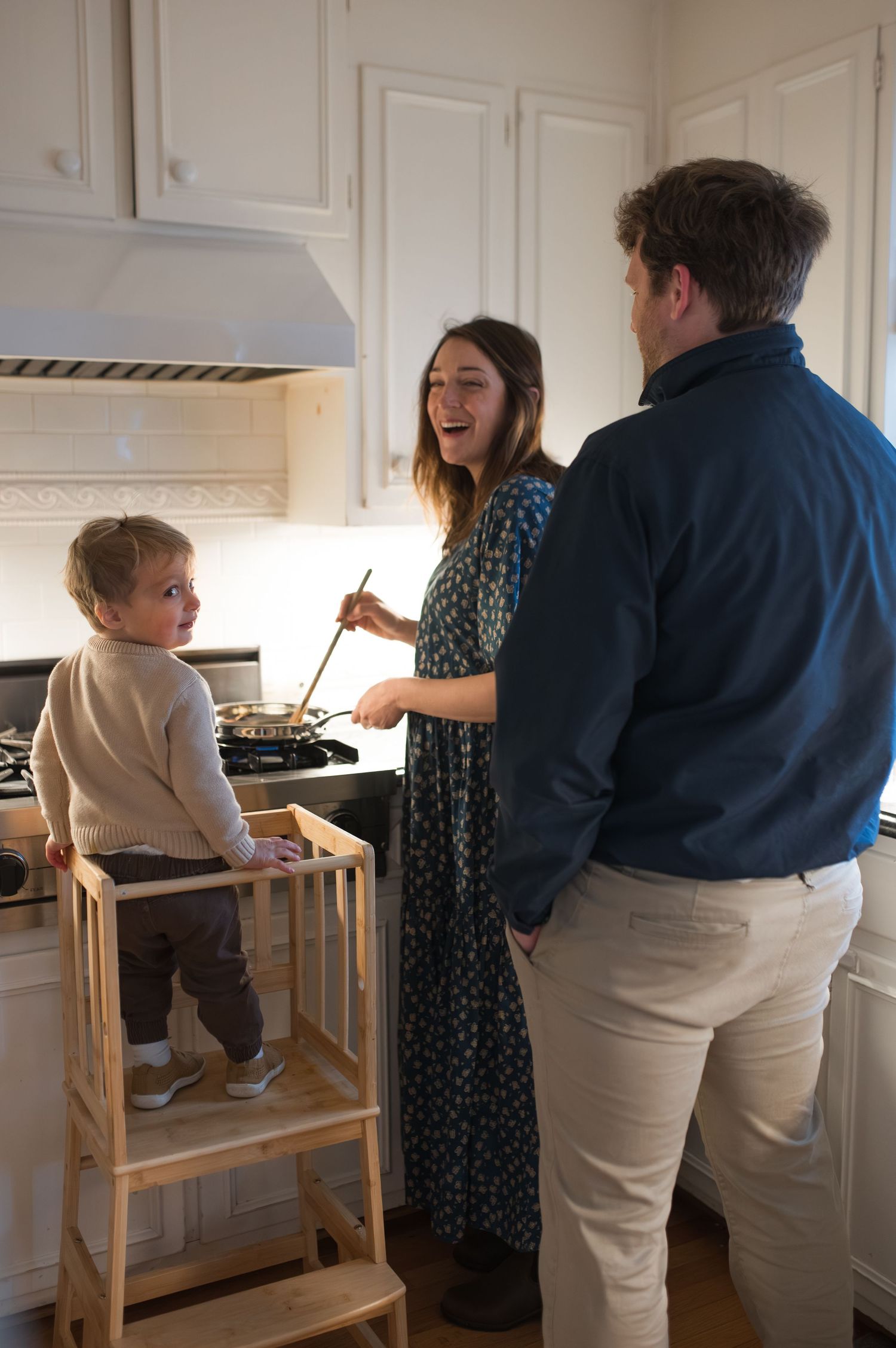 mom dad toddler cooking in kitchen during at-home family session stove oven pot wooden spoon father mother at-home family maternity session