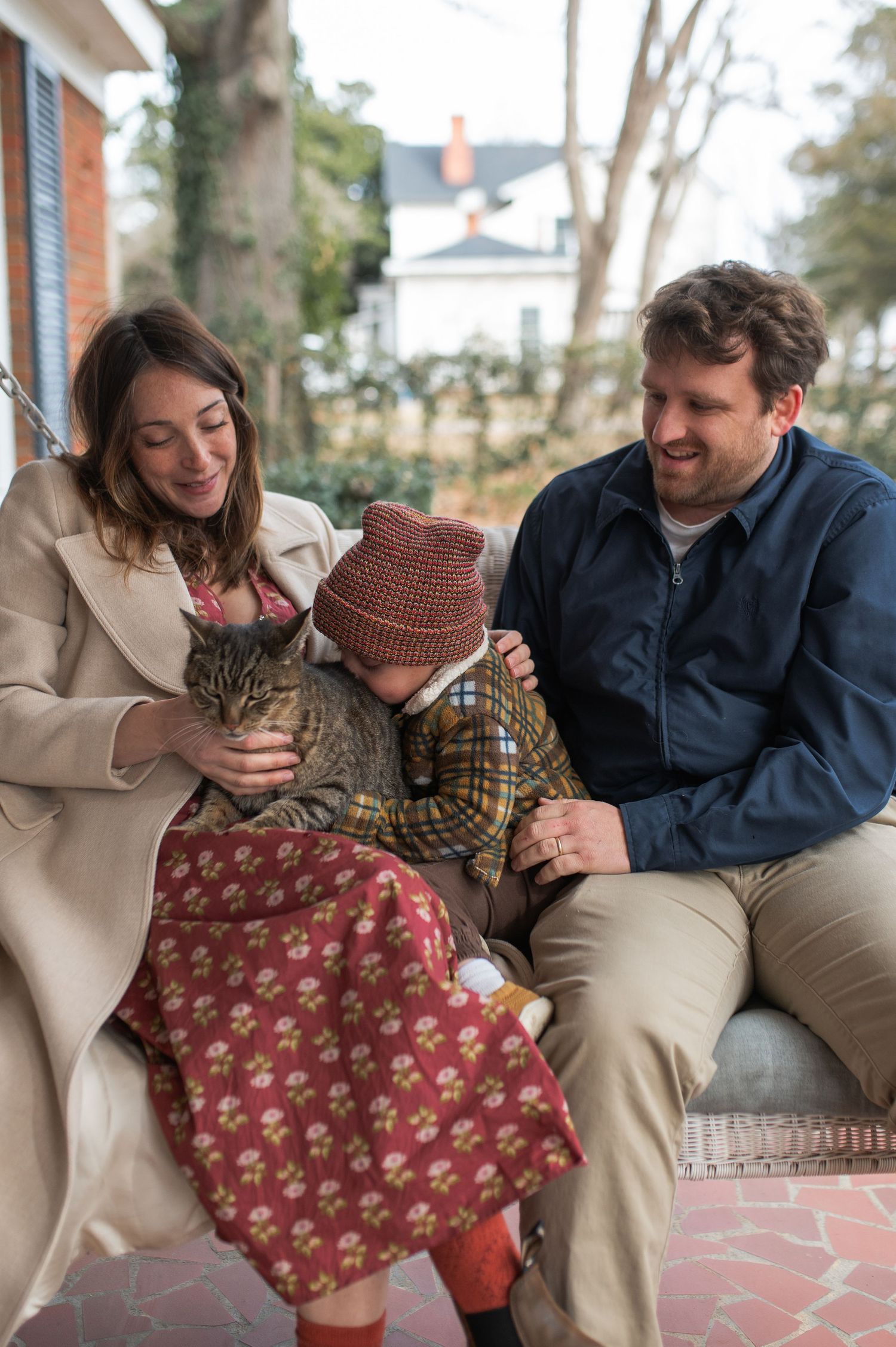 family in porch swing loving on and petting grey brown and black cat at-home family maternity session nc