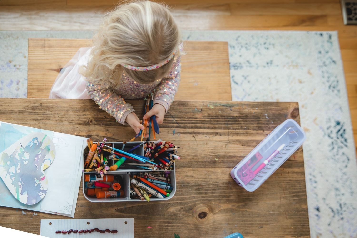child sitting at table, sorting paintbrushes and markers