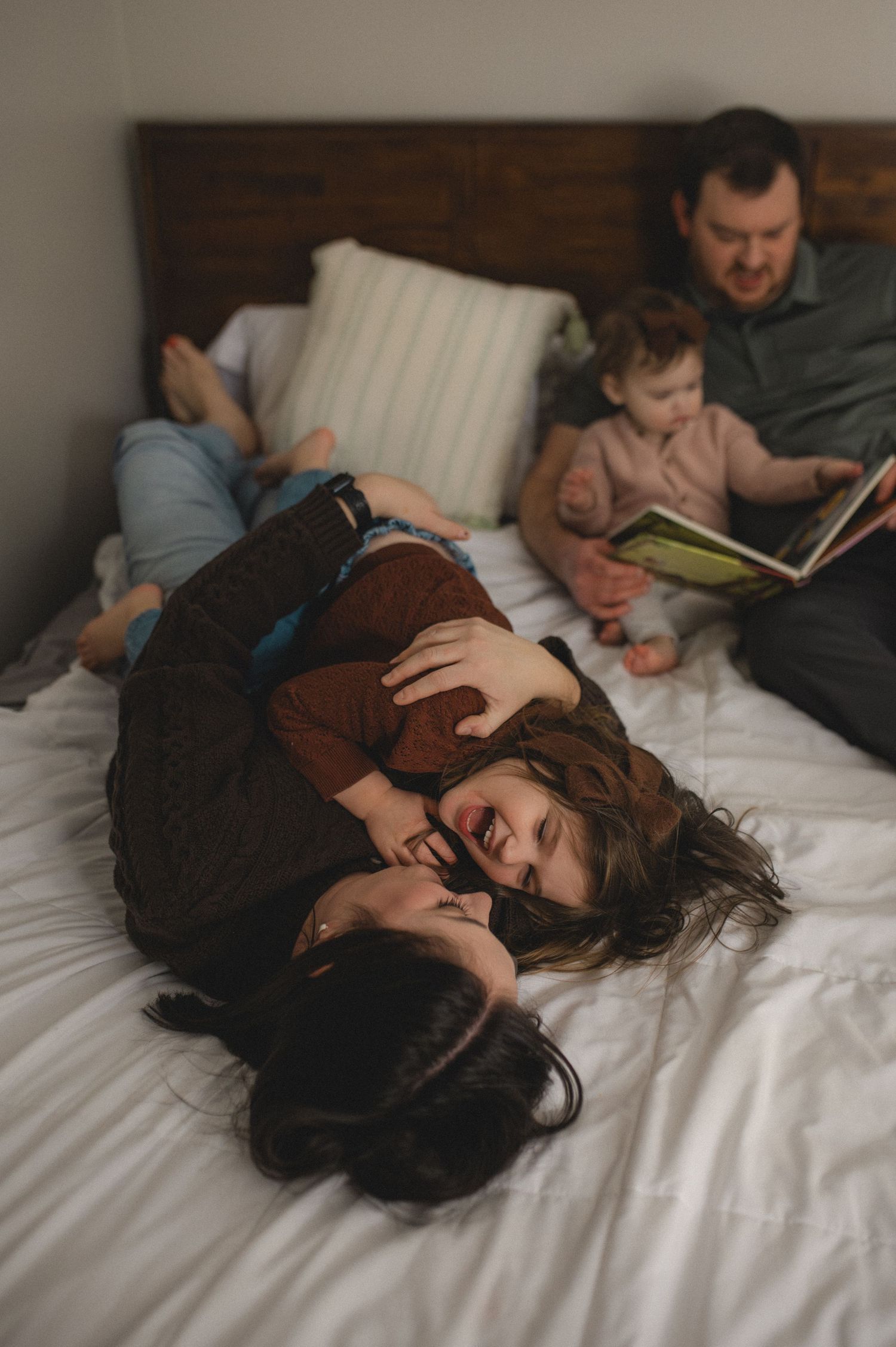 dad and toddler reading book, mom and preschooler playing on bed