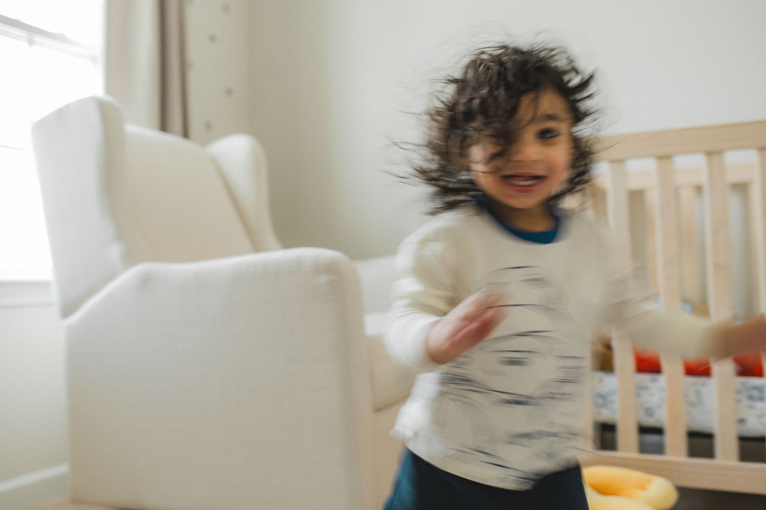 child running, blurry photo, in front of crib and rocking chair