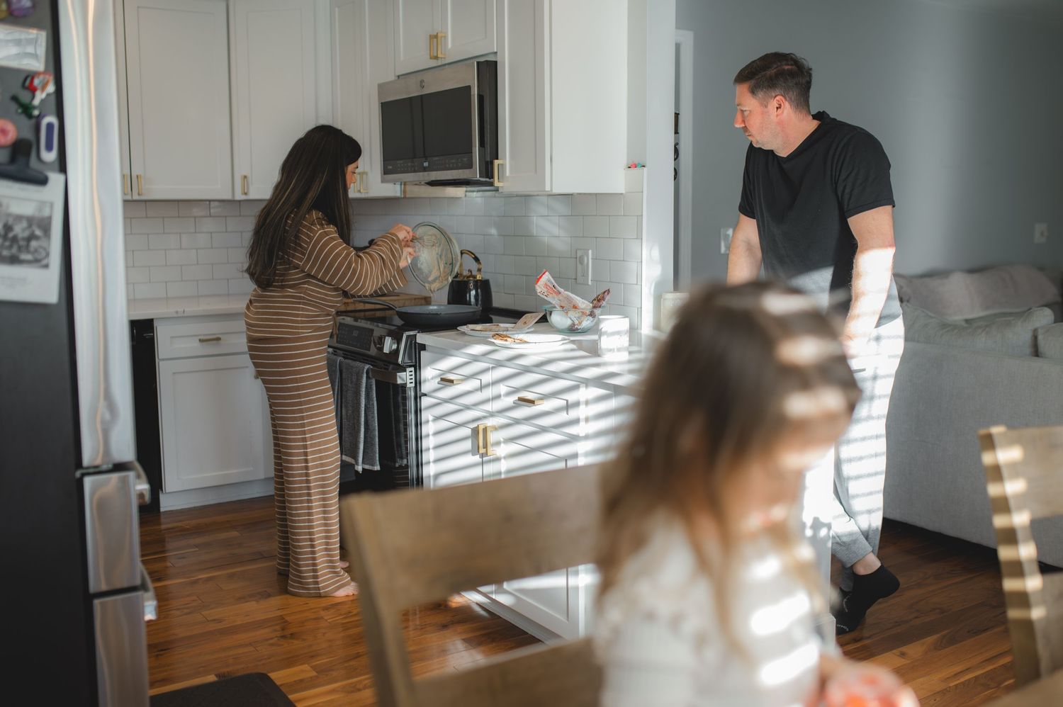 mom and dad in kitchen making pancakes while child sits at table playing, greenville, nc