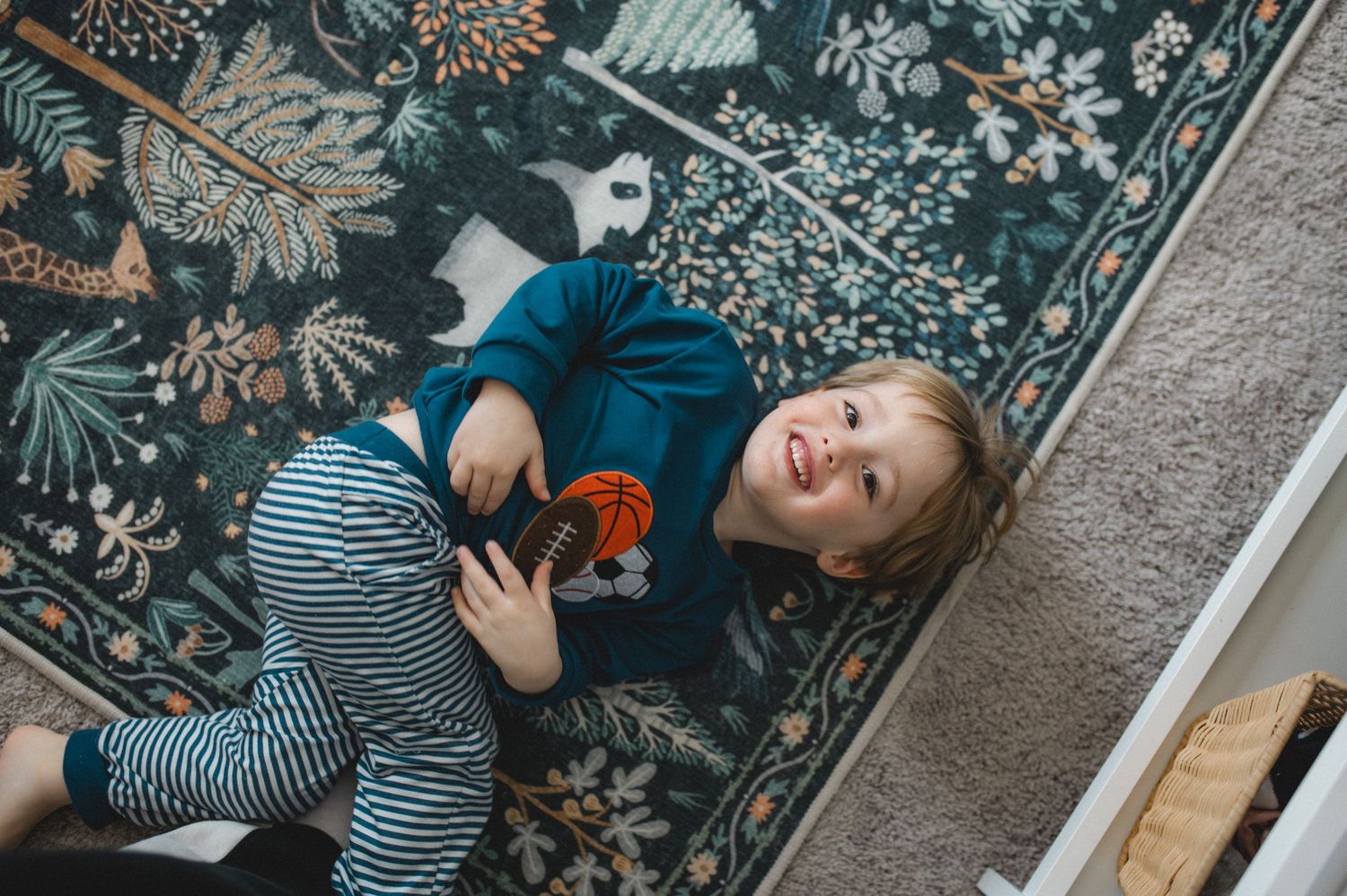 child laying on blue floral floor rug looking up at camera smiling