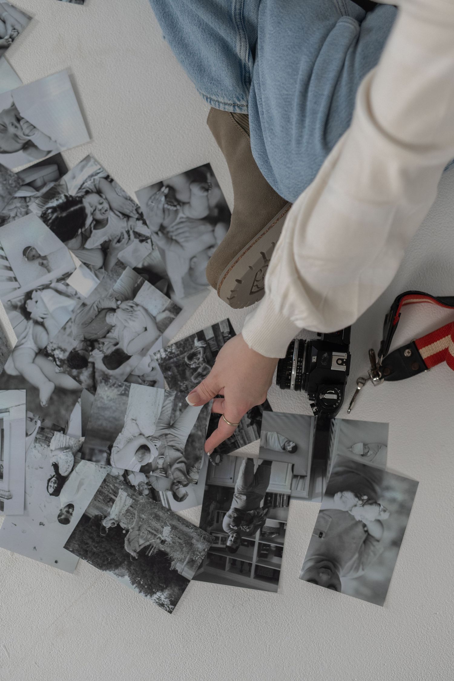 pile of black and white printed photos. hand placing one picture down on top of the others. camera sitting beside foot