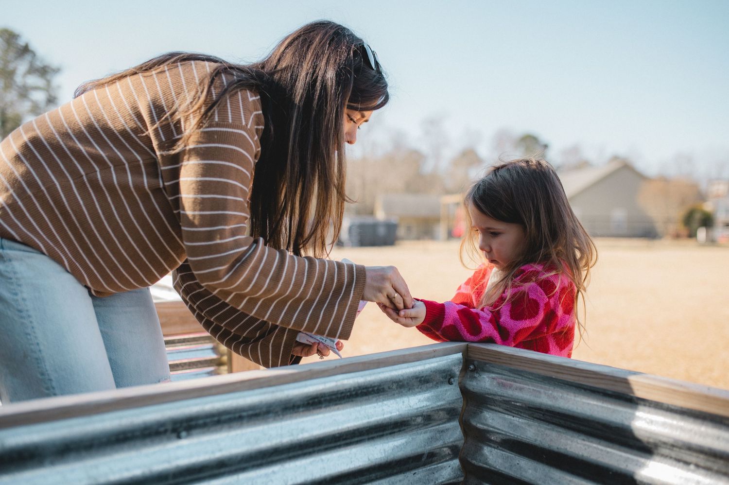 mom and daughter working together to plant seeds in raised garden bed, greenville, nc