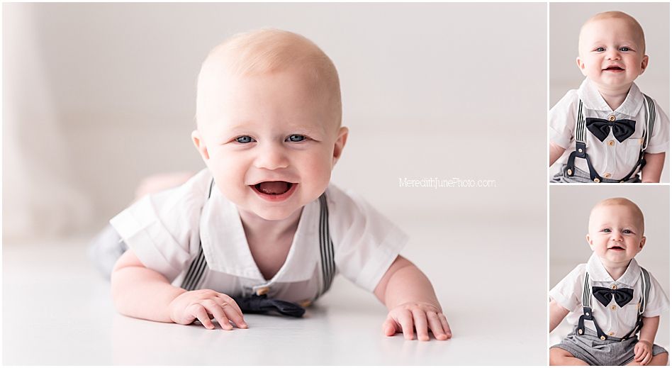 Adorable baby wearing a gray bowtie and suspenders outfit smiles while lying on white floor in studio portraits.