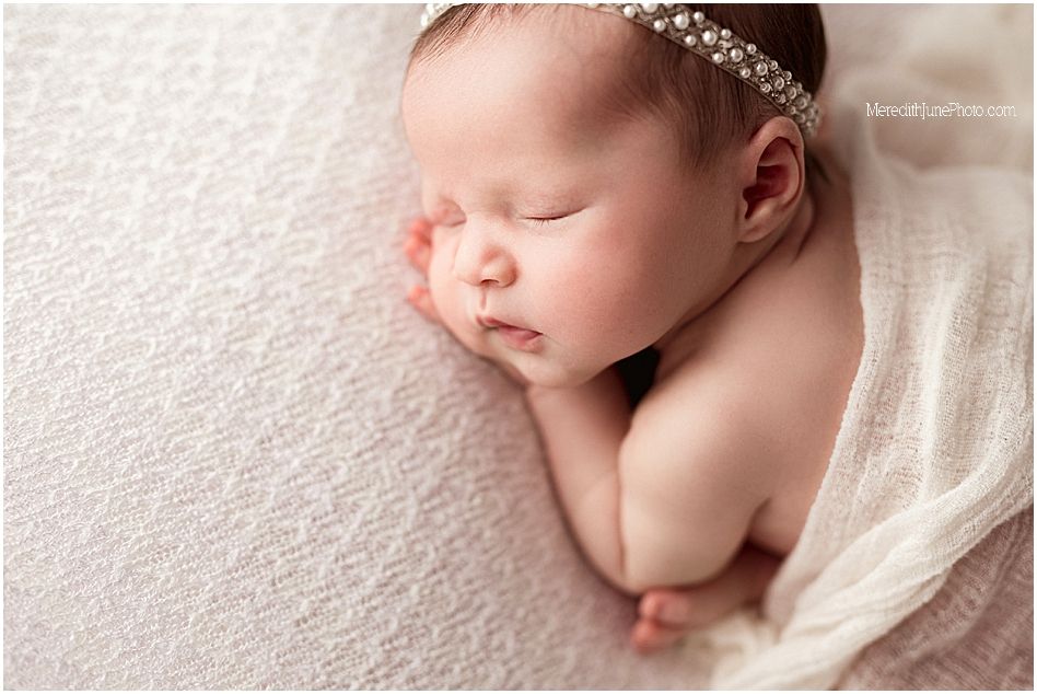 A peaceful newborn baby sleeps on soft white fabric in a minimalist studio photography setting.