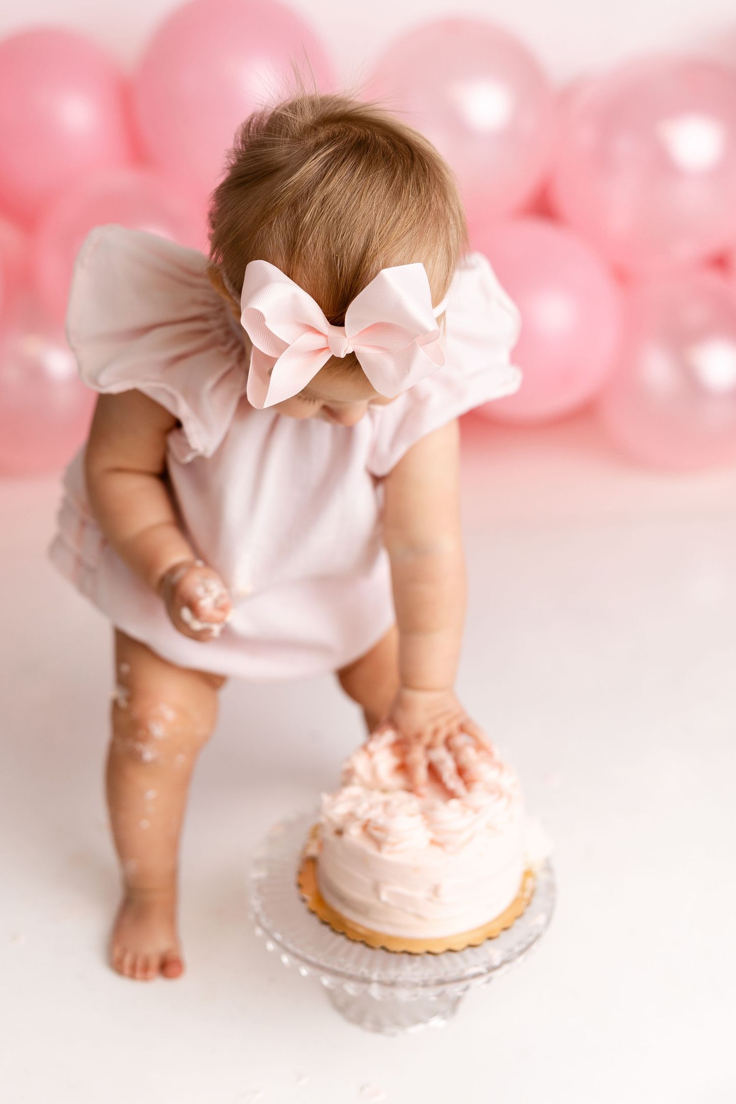 A cake smash photo sequence showing small hands reaching and smashing into a pink frosted cake against a pink background.