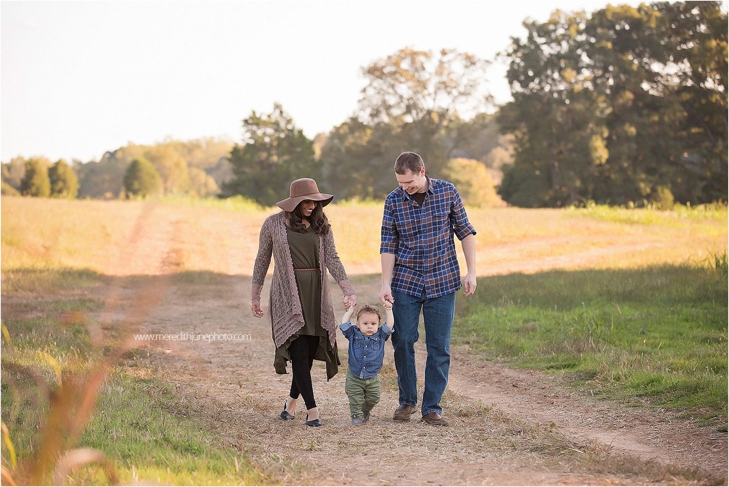 Family walking together on a dirt path through an autumn field at sunset with long shadows cast behind them.