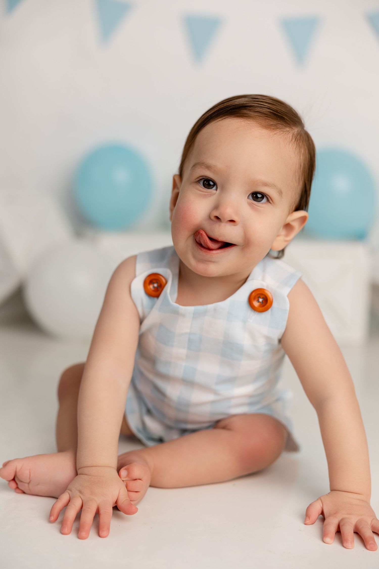 Baby in blue and white outfit crawls on white floor with blue balloon and bunting decorations.