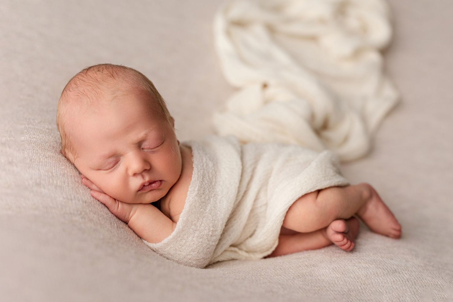 Peaceful newborn sleeping while wrapped in white swaddle on beige background.