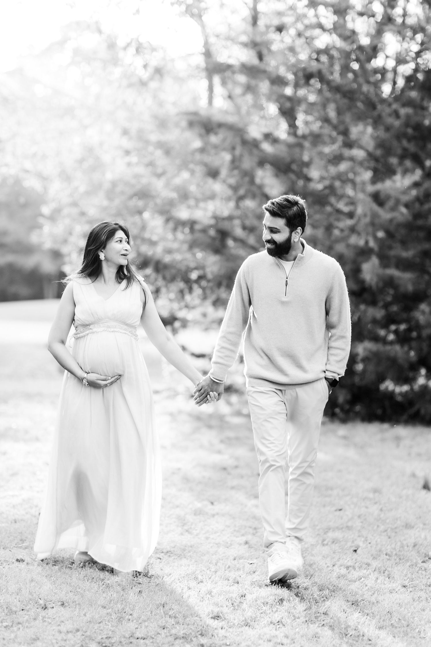 A couple walks hand in hand outdoors in a black and white photo as they await their new arrival.