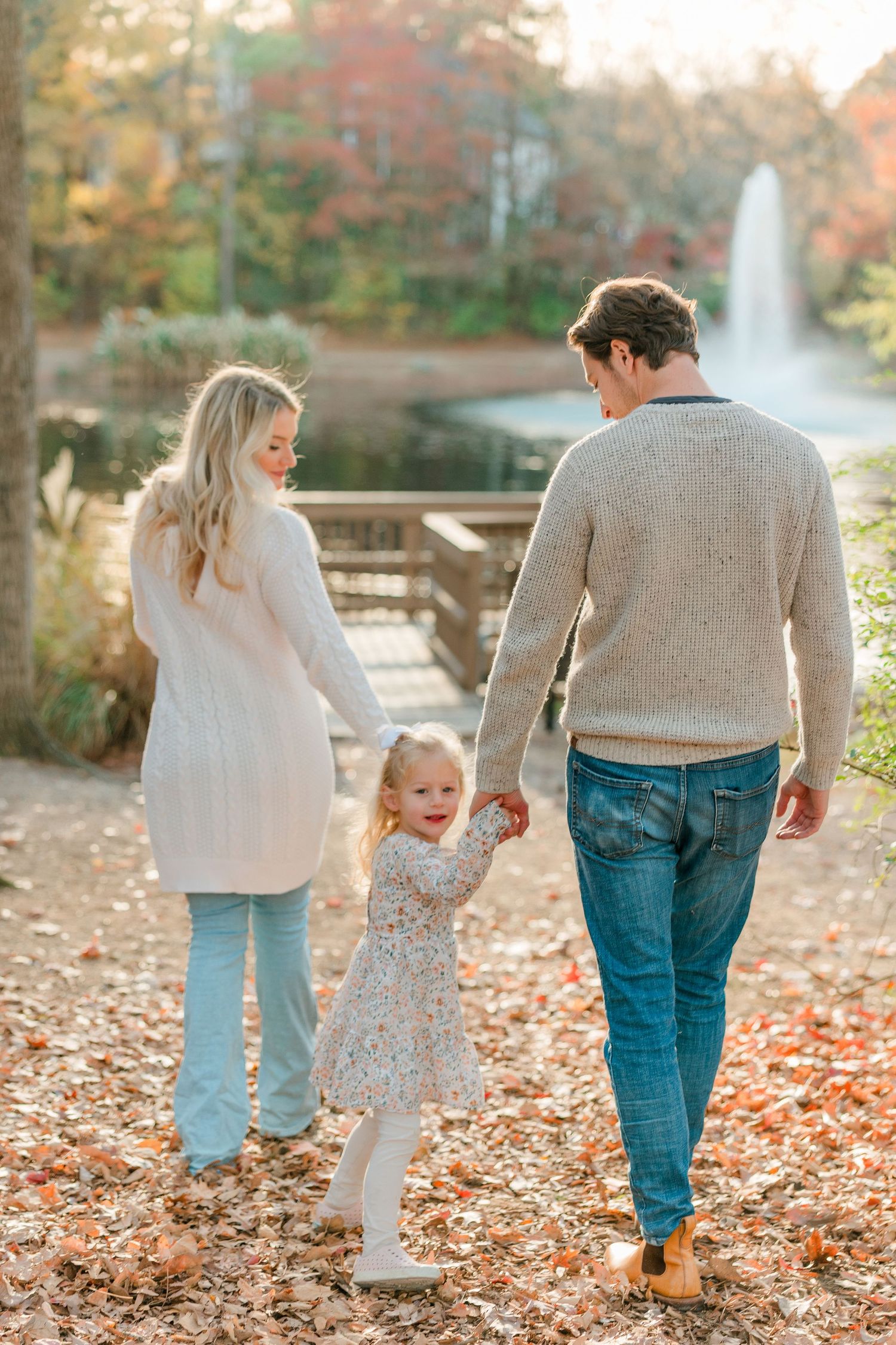 Family walking together through fallen autumn leaves on path.