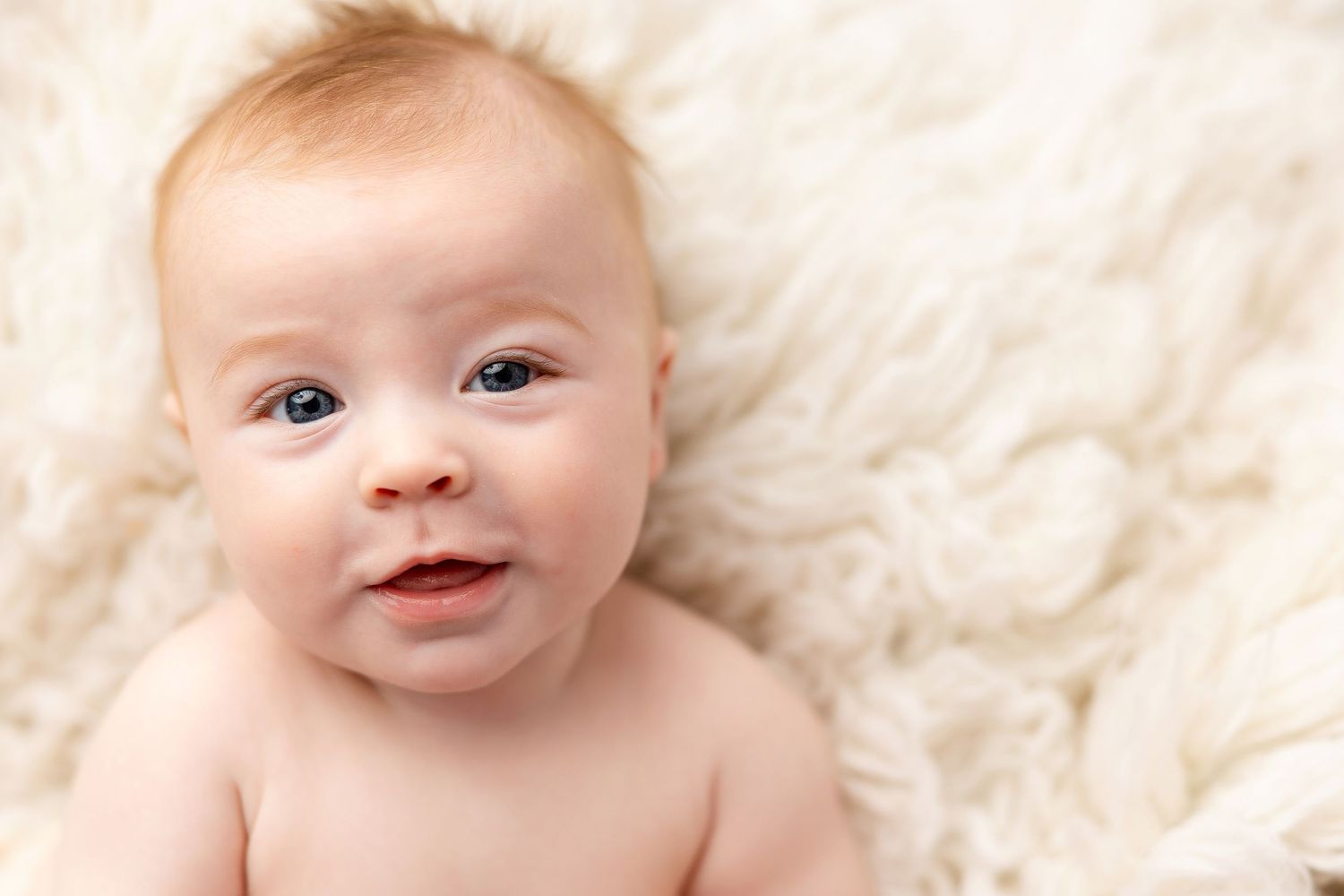 Happy baby lying on soft white textured blanket with bright smile and rosy cheeks.