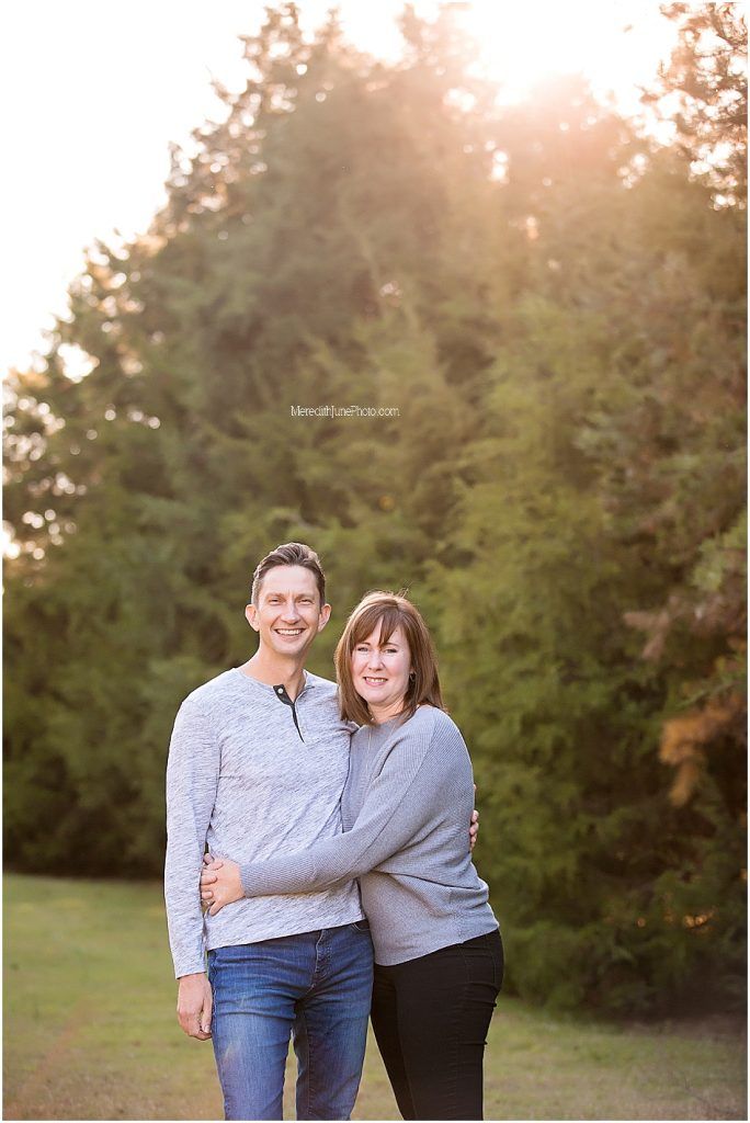A couple poses together outdoors during golden hour with evergreen trees in the background.