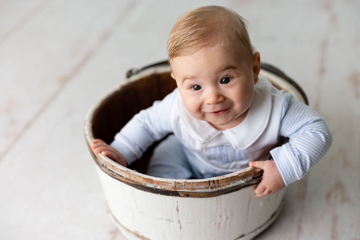 A baby in a white onesie lies on a cozy bed while playing and smiling.