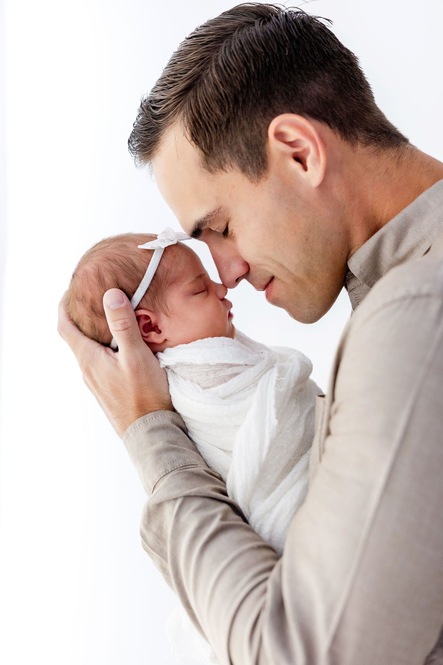 Tender moment captured in profile as parent holds newborn against white background.