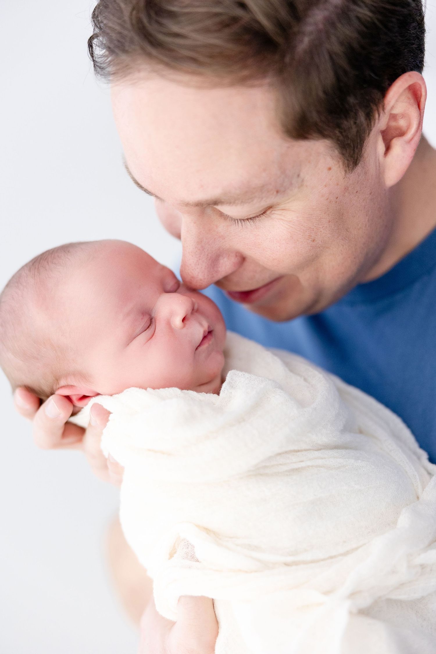 A series of tender close-up photos showing a parent gently kissing a sleeping newborn baby in white.
