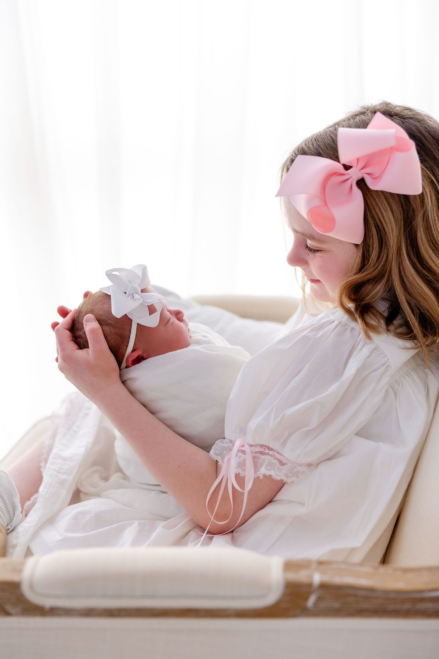 A person in white loungewear and pink bow relaxes on a cream colored couch while reading.