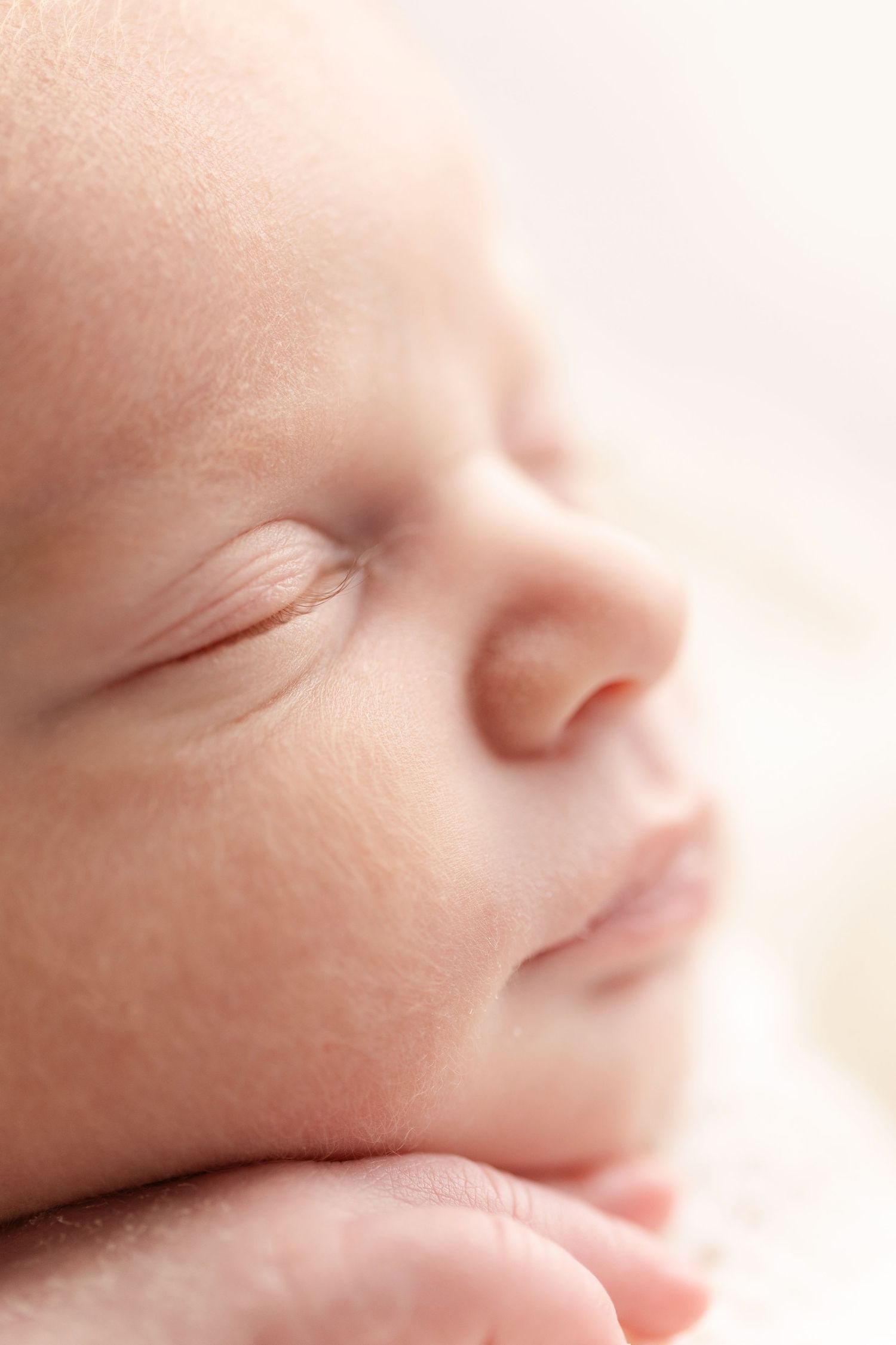 A close-up view of a sleeping newborn baby's face with soft, delicate features in gentle lighting.