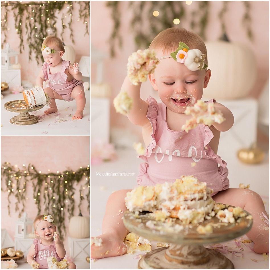 Baby in pink outfit explores cake smash setup with vintage decor and twinkling lights.