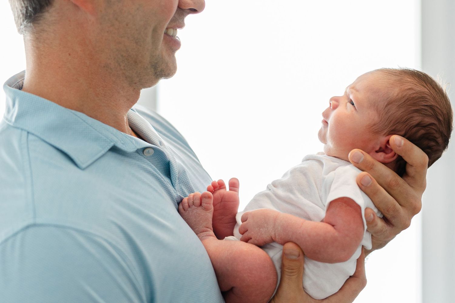 A person in light blue scrubs holds and comforts a crying newborn baby in a medical setting.