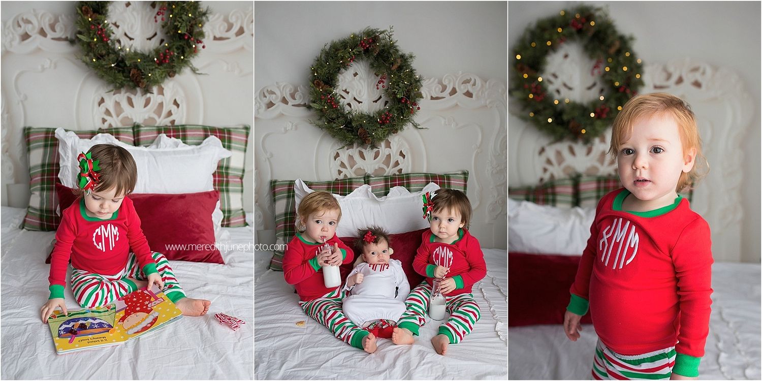 Three children wearing matching red and striped Christmas pajamas sit on a bed beneath a decorative holiday wreath.