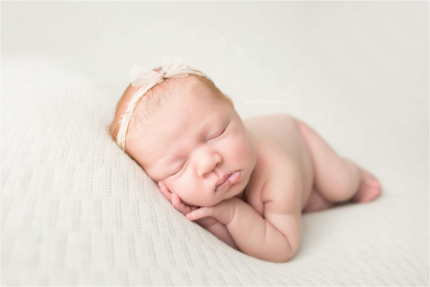 A sleeping newborn baby rests peacefully on soft white bedding during a professional photo session.