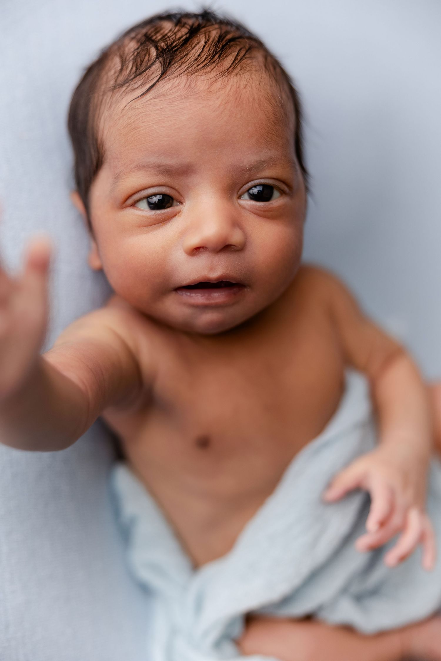 Sweet newborn baby wearing a white diaper smiles and poses during a professional photo session against a light backdrop.
