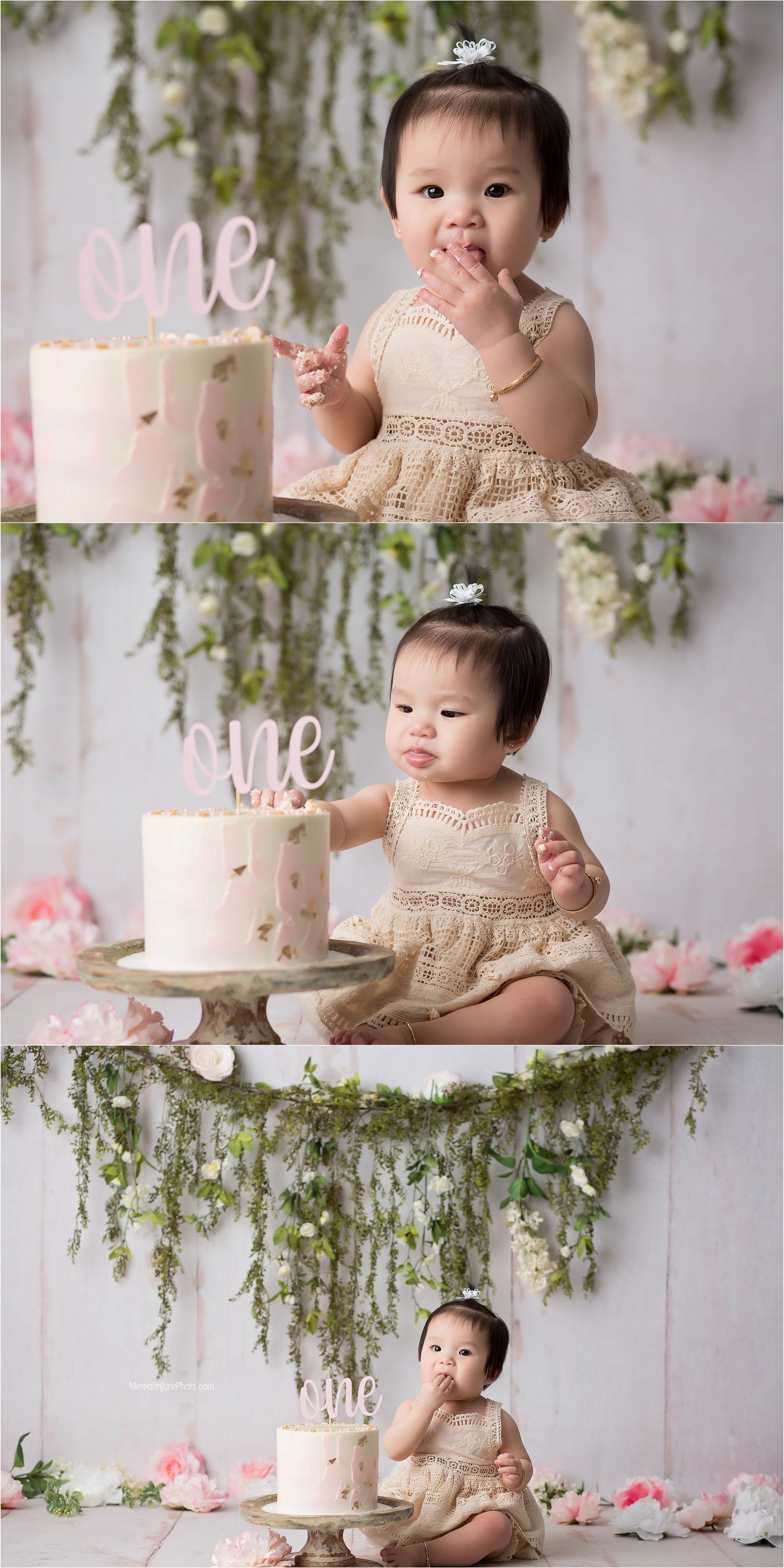 Pink and white birthday cake set against floral backdrop with hanging greenery for special celebration photoshoot.